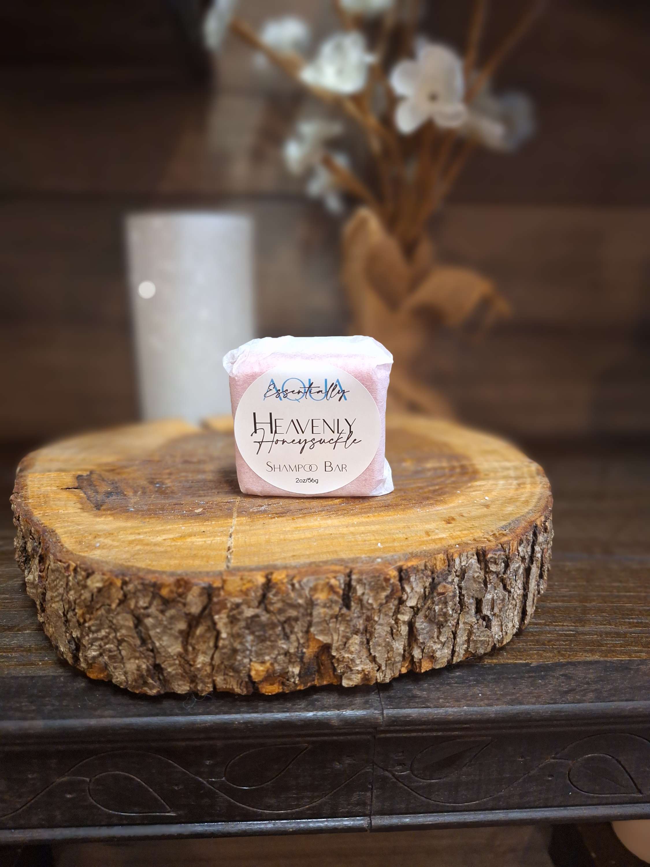 Heavenly Honeysuckle Shampoo Bar on wood slice with candle and flowers in the background.